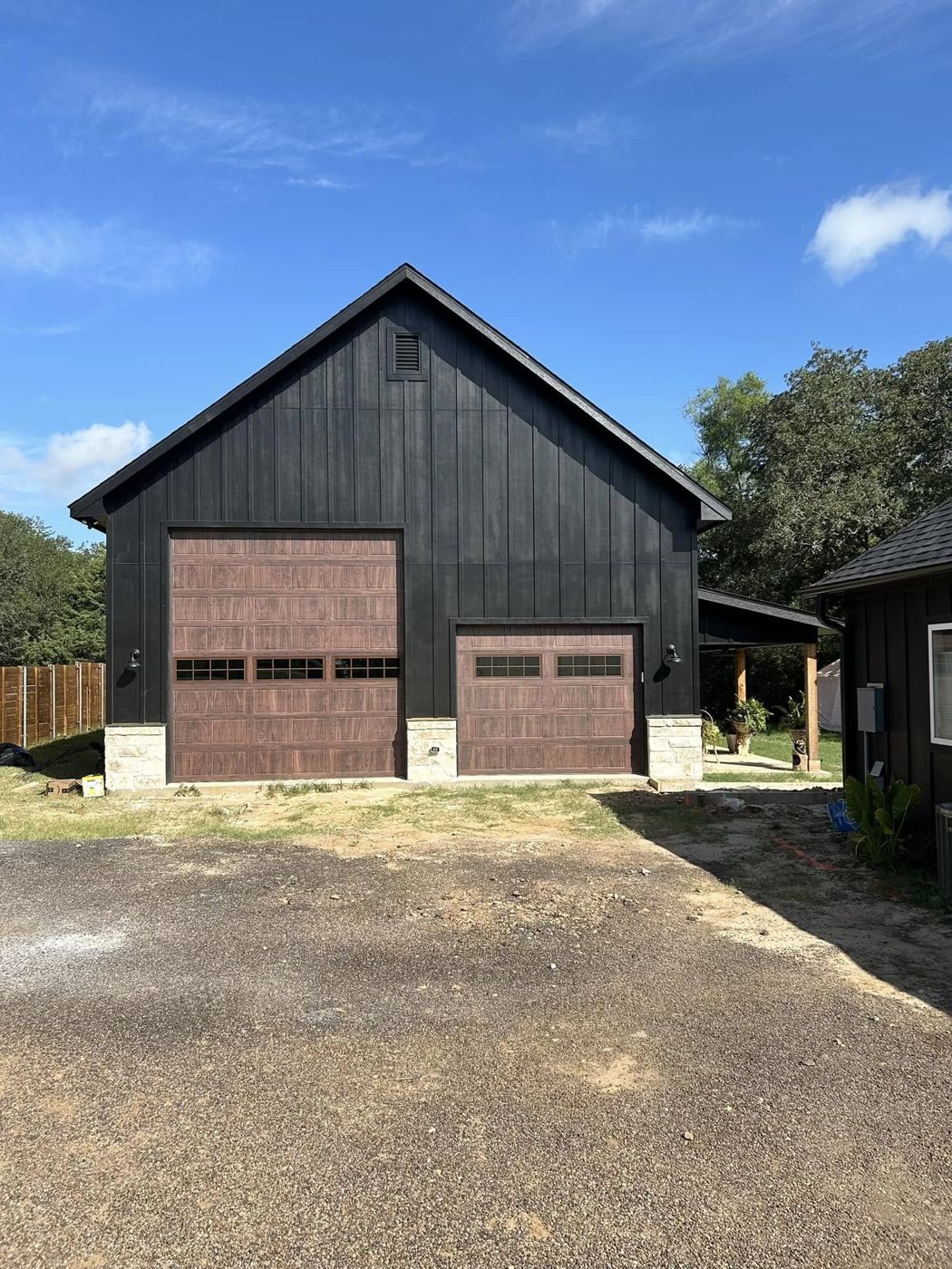 Detached Garage & Shop: Black board-and-batten shop with wood-look garage doors and stone base.