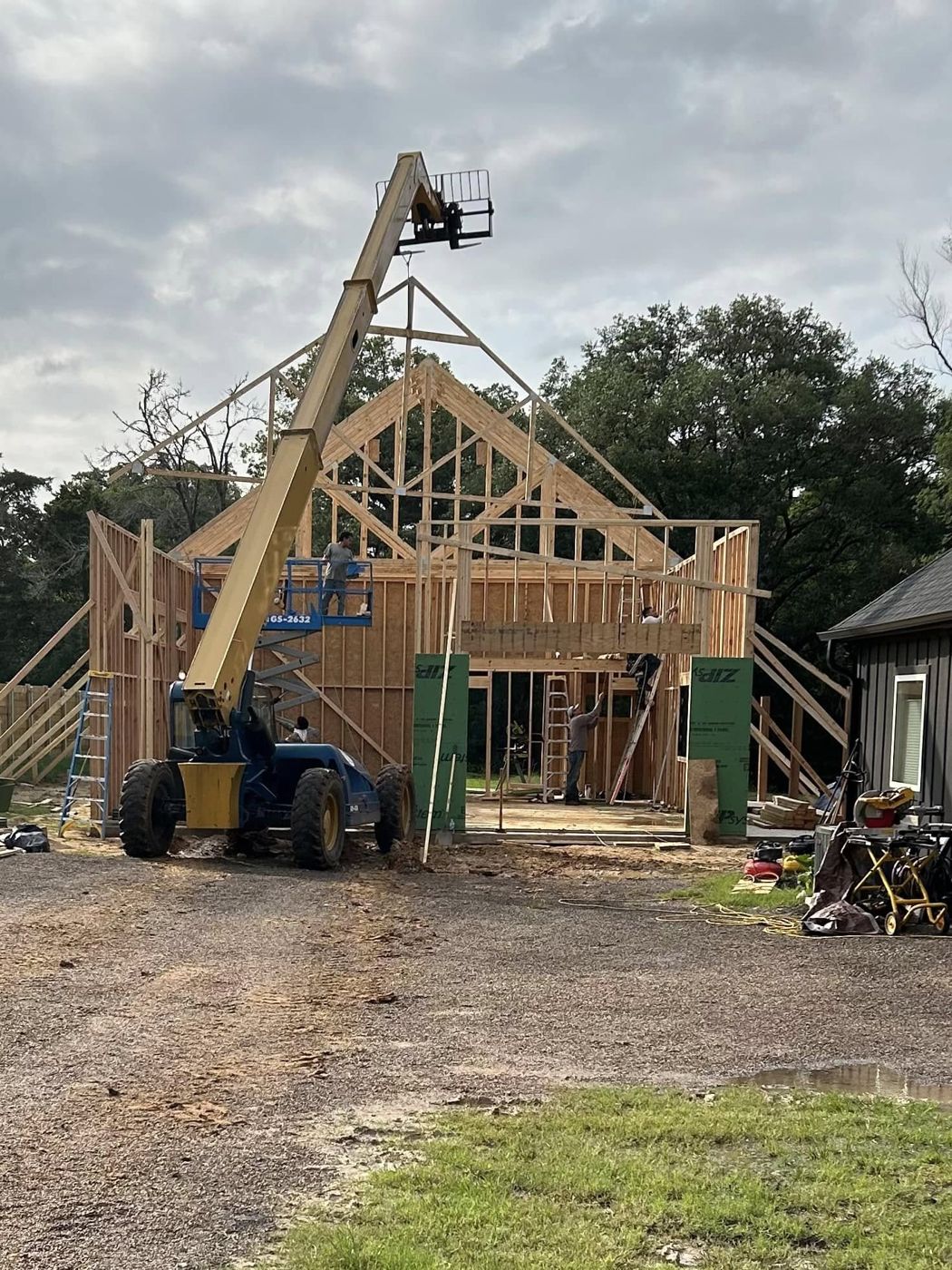 Framing the Shop: Walls up and roof trusses being lifted into place with a telehandler.